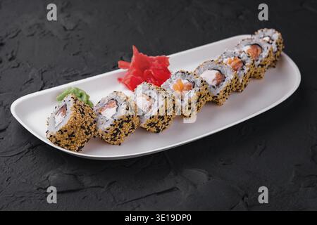 White plate with sushi rolls, ginger, and wasabi on a textured black surface Stock Photo