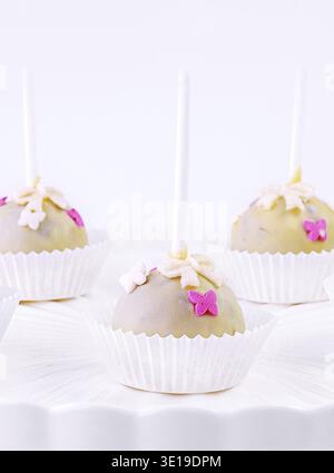 Assorted cake pops with colorful sprinkles displayed on a stylish white cake stand against a clean background Stock Photo