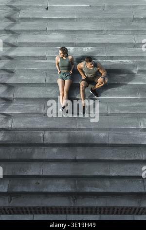 Young athletic couple sitting on concrete staircase after jogging or fitness workout outdoors Stock Photo