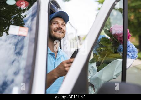 Happy courier inside the white van during flowers delivery is waiting for a client Stock Photo