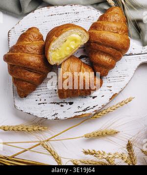 Top view of delicious croissants on a rustic cutting board next to wheat and an open blank book Stock Photo