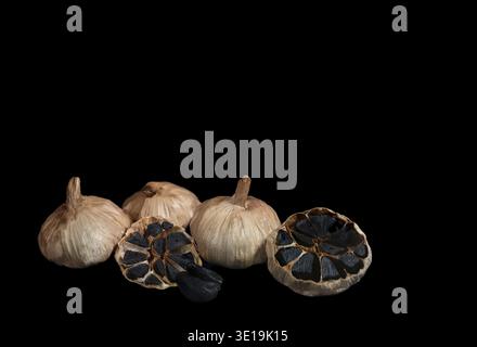 Three whole bulbs of black fermented garlic and one cut crosswise isolated on black Stock Photo