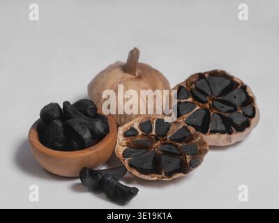Two whole bulbs of black fermented garlic and one cut crosswise and lobules isolated on white very close Stock Photo