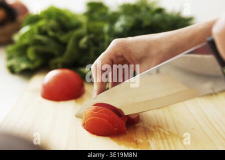 Closeup of female hands with knife slicing red tomato on wooden cutting board Stock Photo
