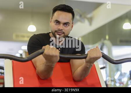 Portrait of young handsome bearded Indian man exercising at the gym Stock Photo