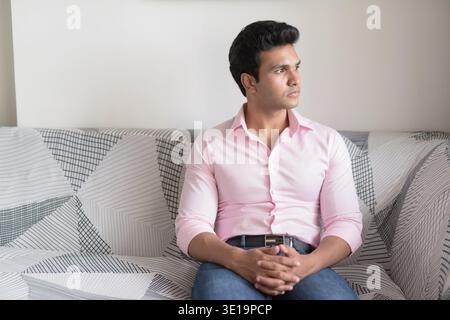 Portrait of young handsome Indian businessman sitting on sofa in the living room at home Stock Photo