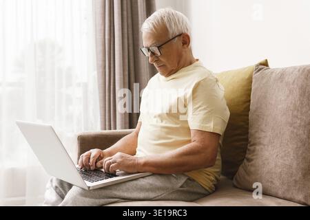 Senior man wearing eyeglasses is using laptop computer at home Stock Photo