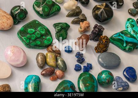 Flat lay view of polished gemstones and mineral pieces arranged on a white surface, featuring green malachite, turquoise stones and various colorful c Stock Photo