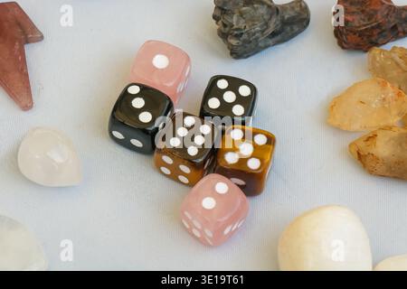Group of colorful gemstone dice placed on a white surface and surrounded by polished mineral stones and crystals, creating a playful tabletop composit Stock Photo
