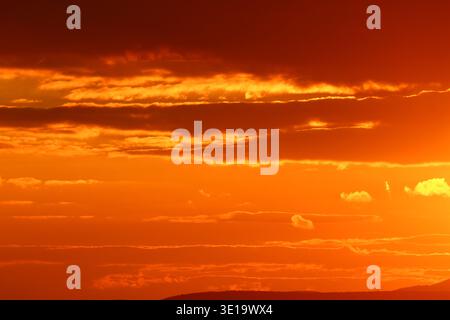 A detailed view of horizontal, wispy clouds illuminated by a deep orange and red fire-like glow in the evening sky. Stock Photo