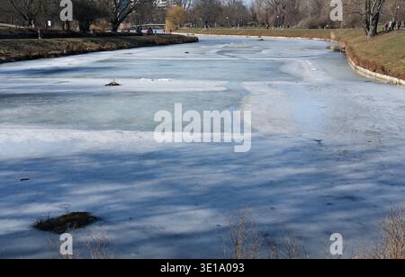 Frozen canal surface with visible cracks and uneven ice texture in a city park Stock Photo