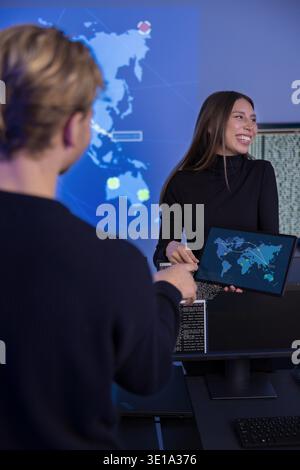 Security professionals collaborating in a technical workspace with threat maps displayed Stock Photo
