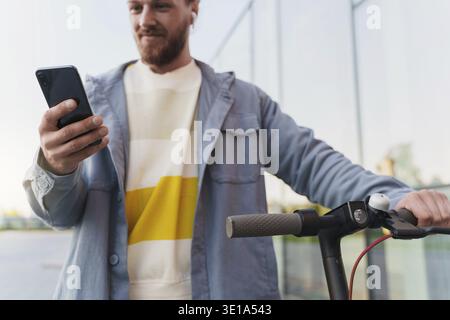 Young man with e-scooter using scooter-sharing system application on his smartphone Stock Photo
