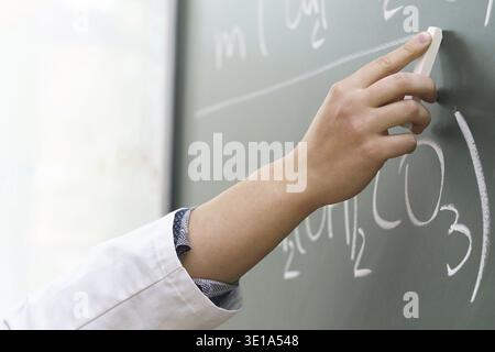 Closeup of scientist hand with a chalk writing a chemical equation Stock Photo