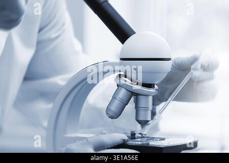 Woman scientist is using immersion oil for microscopy in a laboratory during science research work. Tinted in blue monochrome colors for scientific lo Stock Photo