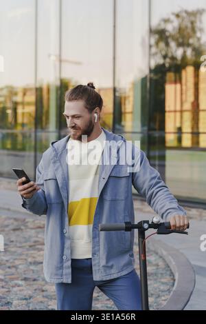 Young man with e-scooter using scooter-sharing system application on his smartphone Stock Photo