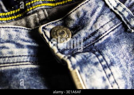 Macro denim jeans button zipper detail showing worn indigo fabric, visible stitching, rivet and faded wash, metallic Stock Photo