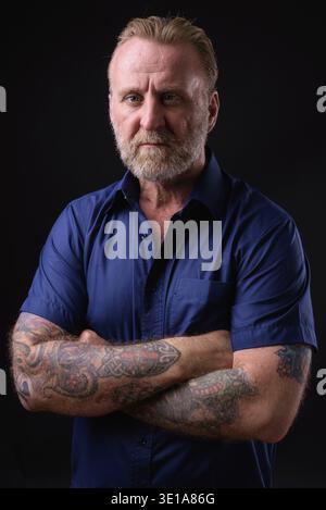 Studio shot of mature handsome bearded man with blond hair against black background Stock Photo
