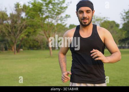Portrait of young handsome bearded Indian man relaxing at the park Stock Photo