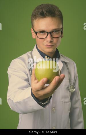Studio shot of young handsome man doctor against green background Stock Photo