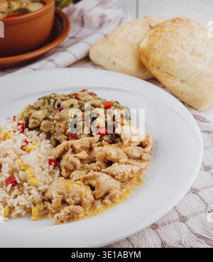 Chicken with rice, eggplant salad and bread on white rustic table setting with a clay pot on the background, representing a healthy home cooked meal Stock Photo
