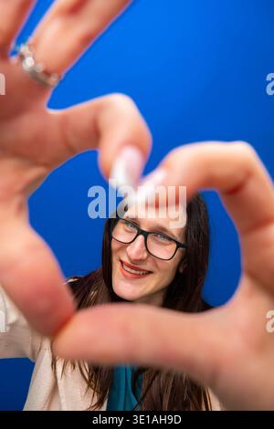 Woman making heart gesture framing smiling face Stock Photo