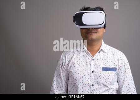 Studio shot of young Indian businessman using virtual reality headset against gray background Stock Photo