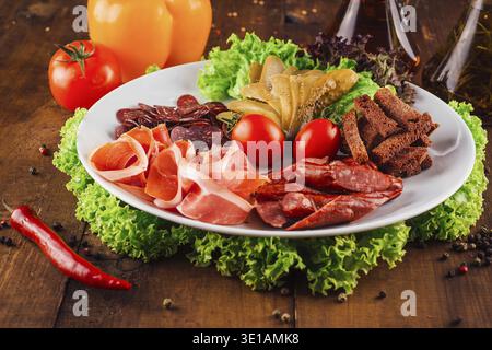 Delicious meat platter with various smoked meats, pickles and rye croutons is served on a wooden table Stock Photo