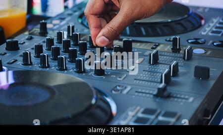 Hand adjusting controls on a DJ mixer controller, creating electronic music at a festival Stock Photo