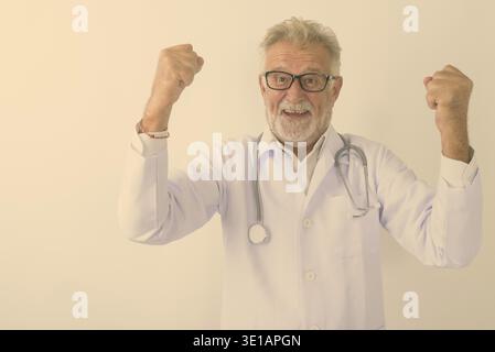 Studio shot of happy senior bearded man doctor smiling while looking excited against white background Stock Photo