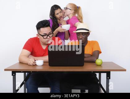 Studio shot of diverse group of multi ethnic friends using laptop with coffee cup and green apple on wooden table together with friends having coffee Stock Photo