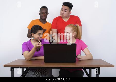 Studio shot of diverse group of multi ethnic friends talking while using laptop on wooden table together Stock Photo