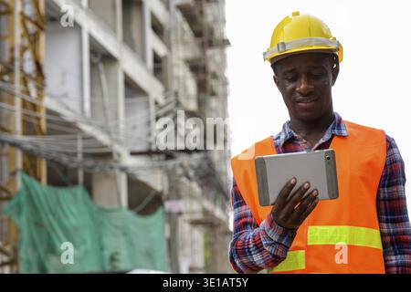 Young happy black African man construction worker smiling while using digital tablet at building site Stock Photo