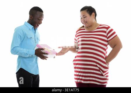 Happy young fat Asian woman giving gift box to young black African man smiling and looking surprised Stock Photo