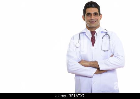 Studio shot of young happy Persian man doctor smiling with arms crossed Stock Photo