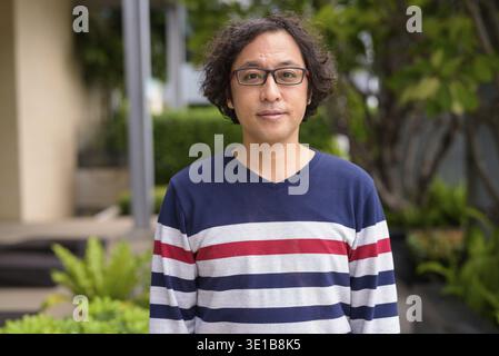 Portrait of Japanese man with curly hair wearing eyeglasses with nature in the rooftop garden outdoors Stock Photo