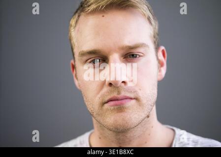Portrait of young handsome man with blond hair against gray background Stock Photo