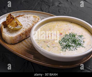 Creamy fish soup served in bowl with bread and grilled lemon on dark background Stock Photo