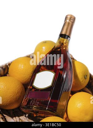 Bottle of cognac with a blank label is laying in a basket full of ripe oranges Stock Photo