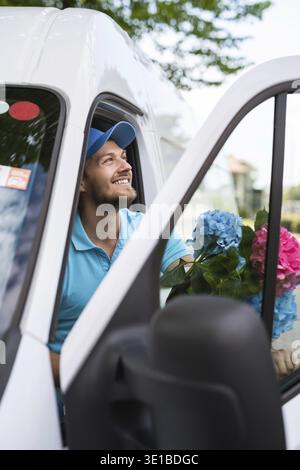 Happy courier inside the white van during flowers delivery is waiting for a client Stock Photo