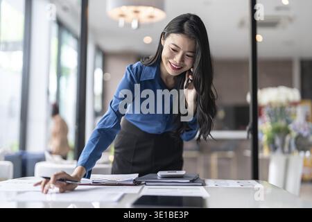 Beautiful confident asian secretary woman clever smart professional business woman talking on phone in office Stock Photo