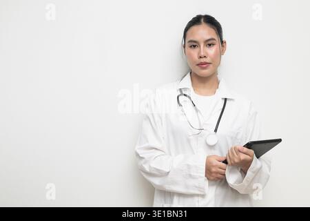 Portrait of a young Thai female doctor in a white medical uniform using a digital tablet computer with a stethoscope on plain background, suitable for Stock Photo