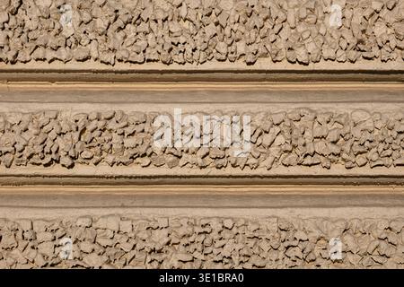 Rough concrete wall displaying aggregated pebble texture and horizontal stucco bands Stock Photo