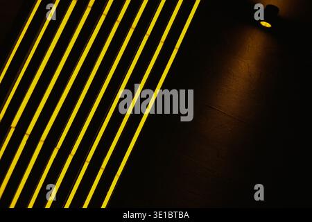 A professional abstract shot featuring rhythmic diagonal lines of vibrant yellow neon lighting. The composition is balanced by a single spotlight cast Stock Photo