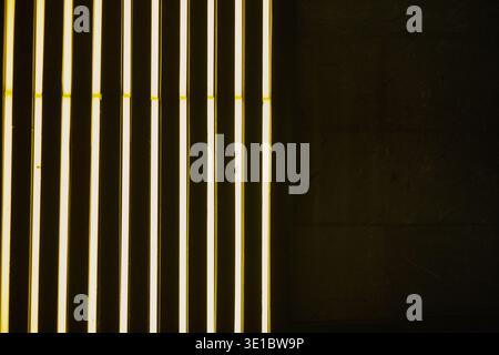 A professional abstract shot featuring rhythmic diagonal lines of vibrant yellow neon lighting. The composition is balanced by a single spotlight cast Stock Photo