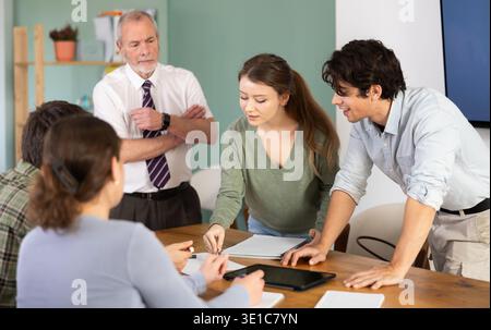 Students solving problems at table with teacher in background Stock Photo
