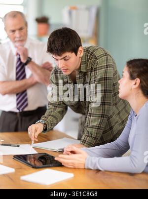 Students solving problems at table with teacher in background Stock Photo