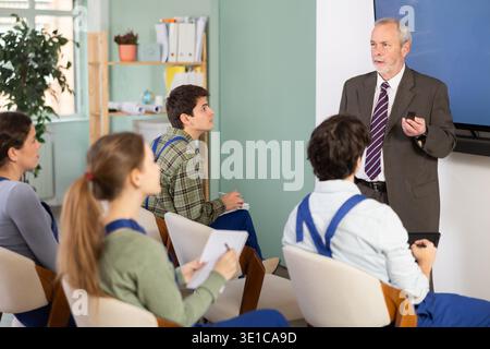 Senior teacher holding a remote control and speaking to student audience Professional senior teacher holding a remote control and speaking to student Stock Photo