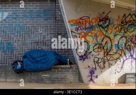 Homeless person sleeping rough under a bridge next to graffiti in Guildford, Surrey, England, UK Stock Photo