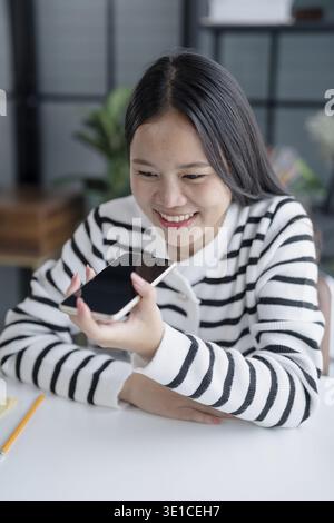 Asian Woman Engaging with Voice Assistant on Smartphone in Modern Home Stock Photo